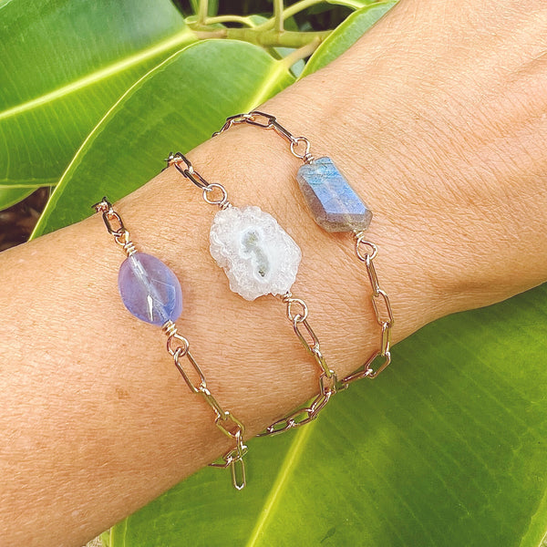 Female wrist wearing 3 paperclip chain bracelets each featuring a different polished focal crystal: Blue opalite, solar quartz & labradorite