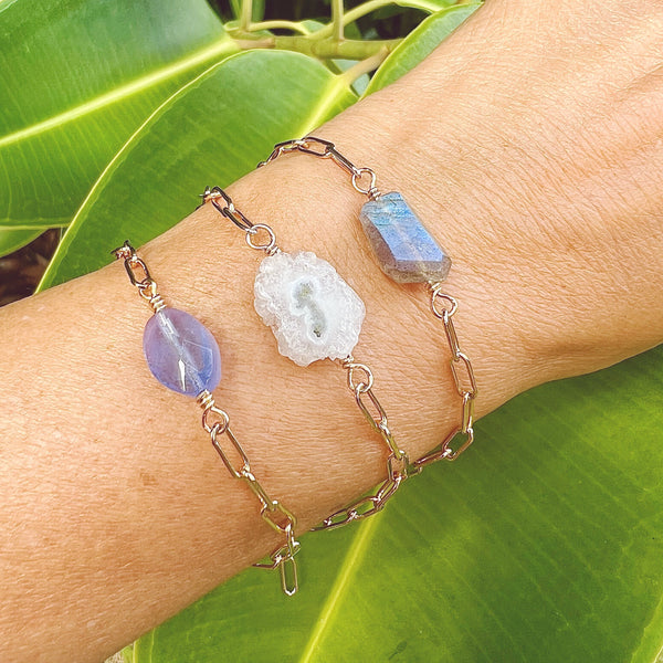 Female wrist wearing 3 paperclip chain bracelets each featuring a different polished focal crystal: Blue opalite , solar quartz & labradorite